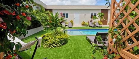 A modern pool area with artificial grass, lounge chairs, and a wooden lattice structure.