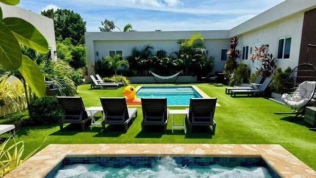 Piscina com hidromassagem em primeiro plano, rodeada por espreguiçadeiras e um gramado.