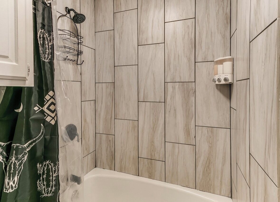 Une salle de bain avec un carrelage disposé en motif de chevron, une pomme de douche et un porte-serviettes.