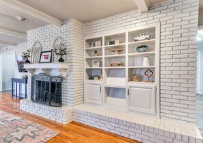 Una sala de estar con chimenea de ladrillo blanco, estanterías empotradas y un tapete estampado.