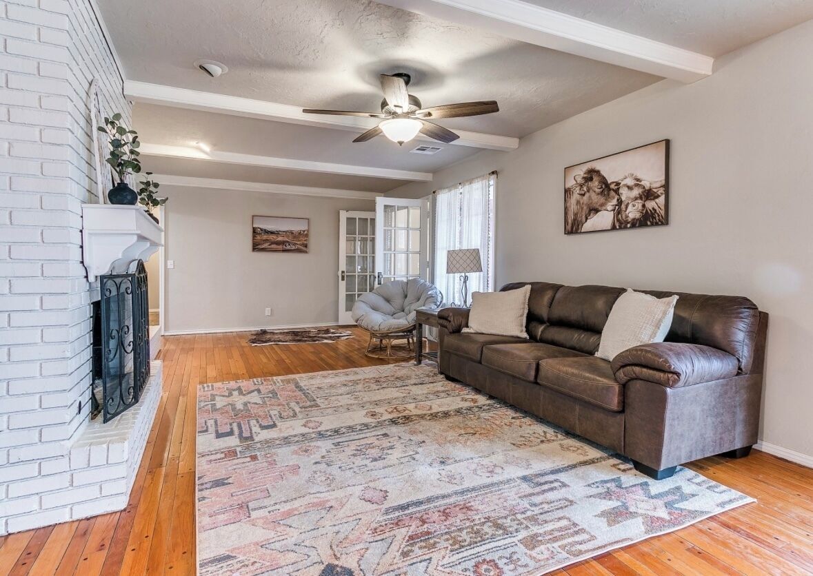 A living room with a brown leather sofa, a patterned rug, a fireplace, and a ceiling fan.