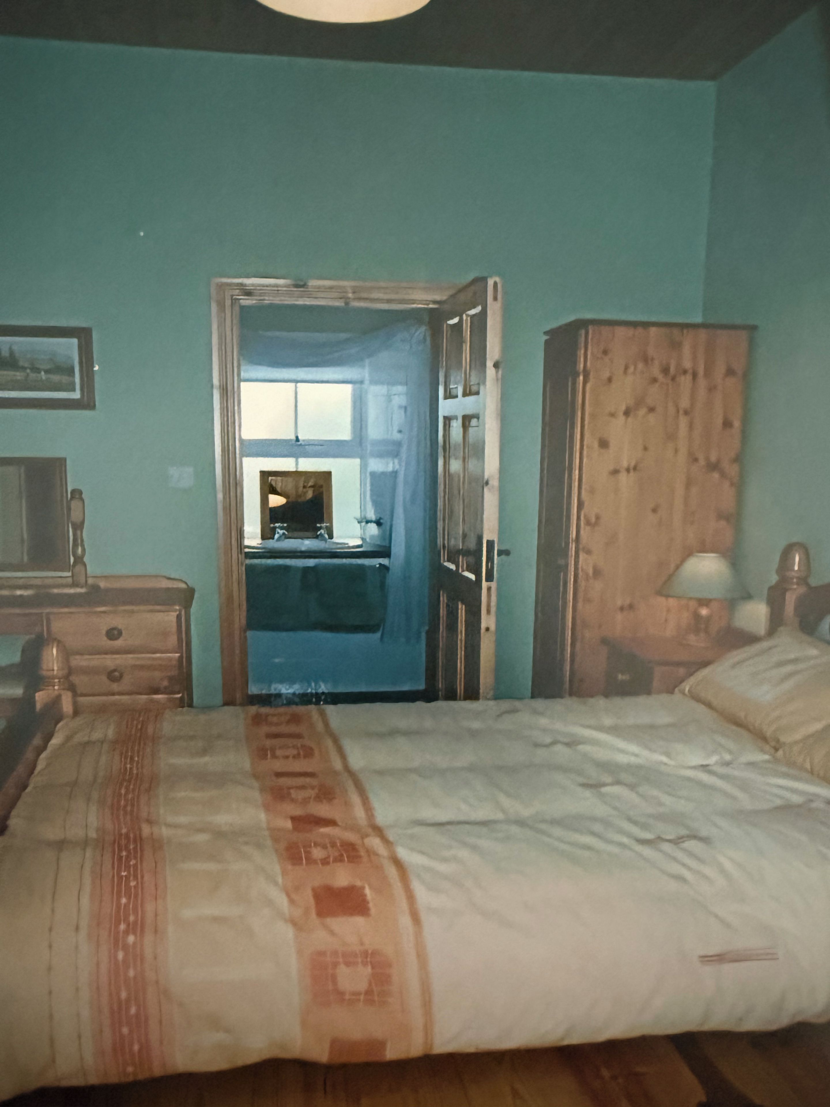 A bedroom with a bed, a wooden wardrobe, a desk, and a chair.