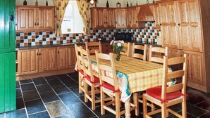 Una cocina con armarios de madera, salpicadero de azulejos, una mesa de comedor con sillas y un refrigerador verde.
