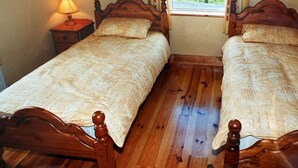 Una habitación con dos camas de madera con cabeceras y pies de cama a juego, una mesita de noche con una lámpara y una ventana con cortinas.