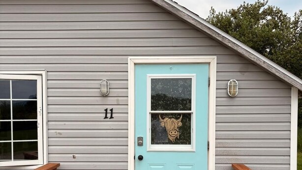 A house with a light blue door, a number 11 sign, and a wooden deck with a 'hello' mat.