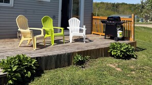A house with a deck, three Adirondack chairs, a grill, and a barbecue.