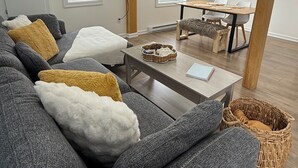 A modern living room with a grey sofa, a wooden coffee table, and a dining area with a table and chairs.