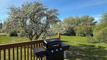 Enjoy outdoor cooking on the deck with a portable grill and lush green surroundings.