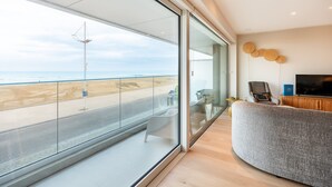 A modern living room with a large glass door leading to a balcony overlooking a beach.