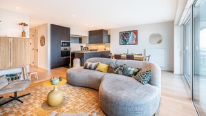 A modern living room with a grey sectional sofa, a small round table, and a dining area with a wooden table and chairs.