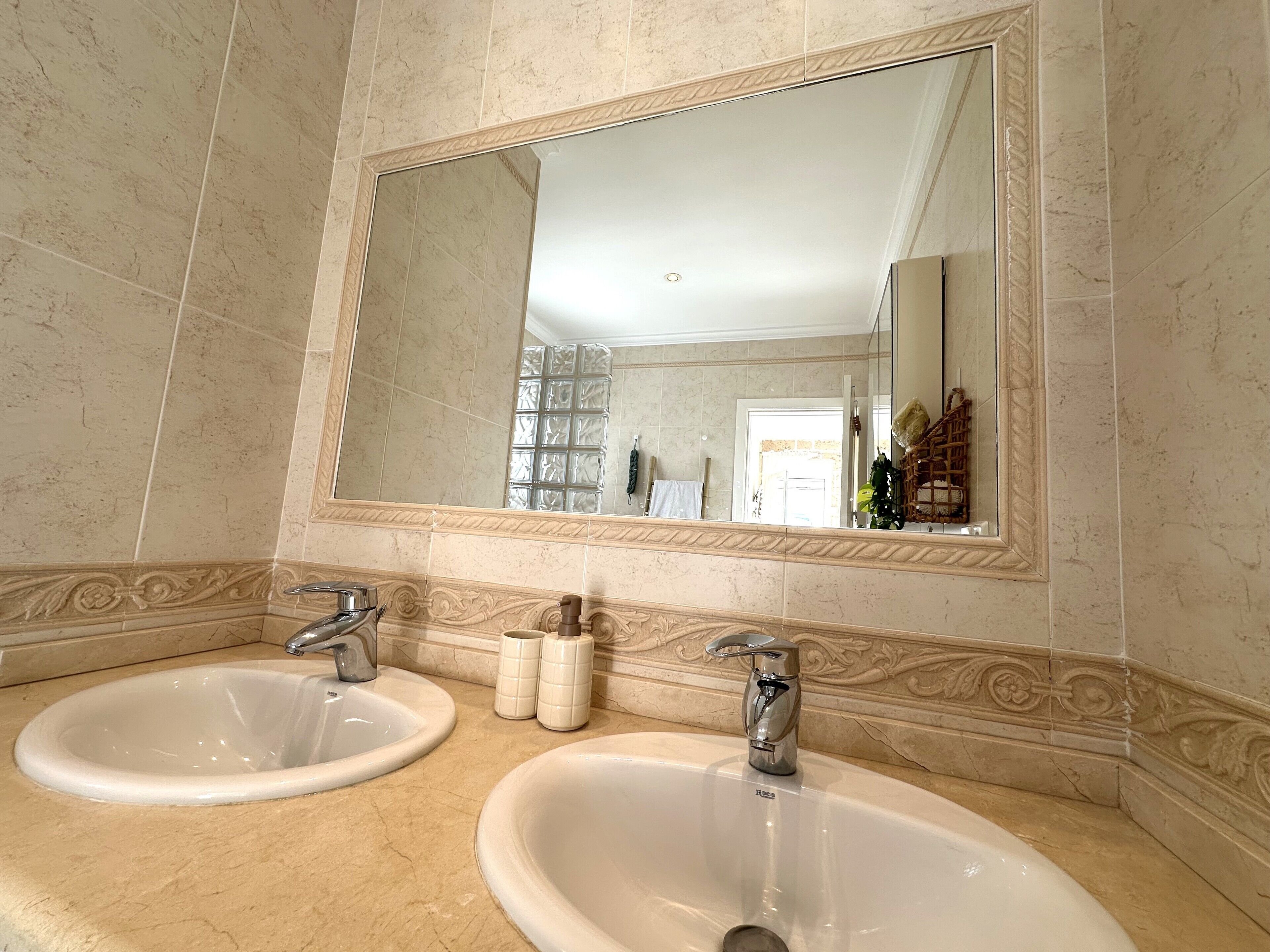 Un baño con dos lavamanos, un espejo grande y azulejos decorativos en la pared.