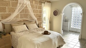 A bedroom with a bed, a nightstand, a bedside lamp, a decorative wall piece, and a view of the outside through a window. - Villa Casa Creativa: your sunny dream holiday home with breathtaking sea views (El Poble Nou de Benitatxell)