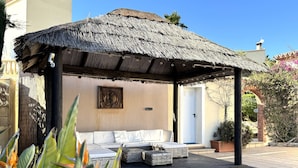 A thatched-roof outdoor seating area with a sofa and cushions, a Buddha statue, and a potted plant. - Villa Casa Creativa: your sunny dream holiday home with breathtaking sea views (El Poble Nou de Benitatxell)