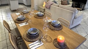 A dining area with a wooden table set for six, surrounded by wicker chairs. There is a lit candle on the table, and a kitchen is visible in the background. - Villa Casa Creativa: your sunny dream holiday home with breathtaking sea views (El Poble Nou de Benitatxell)