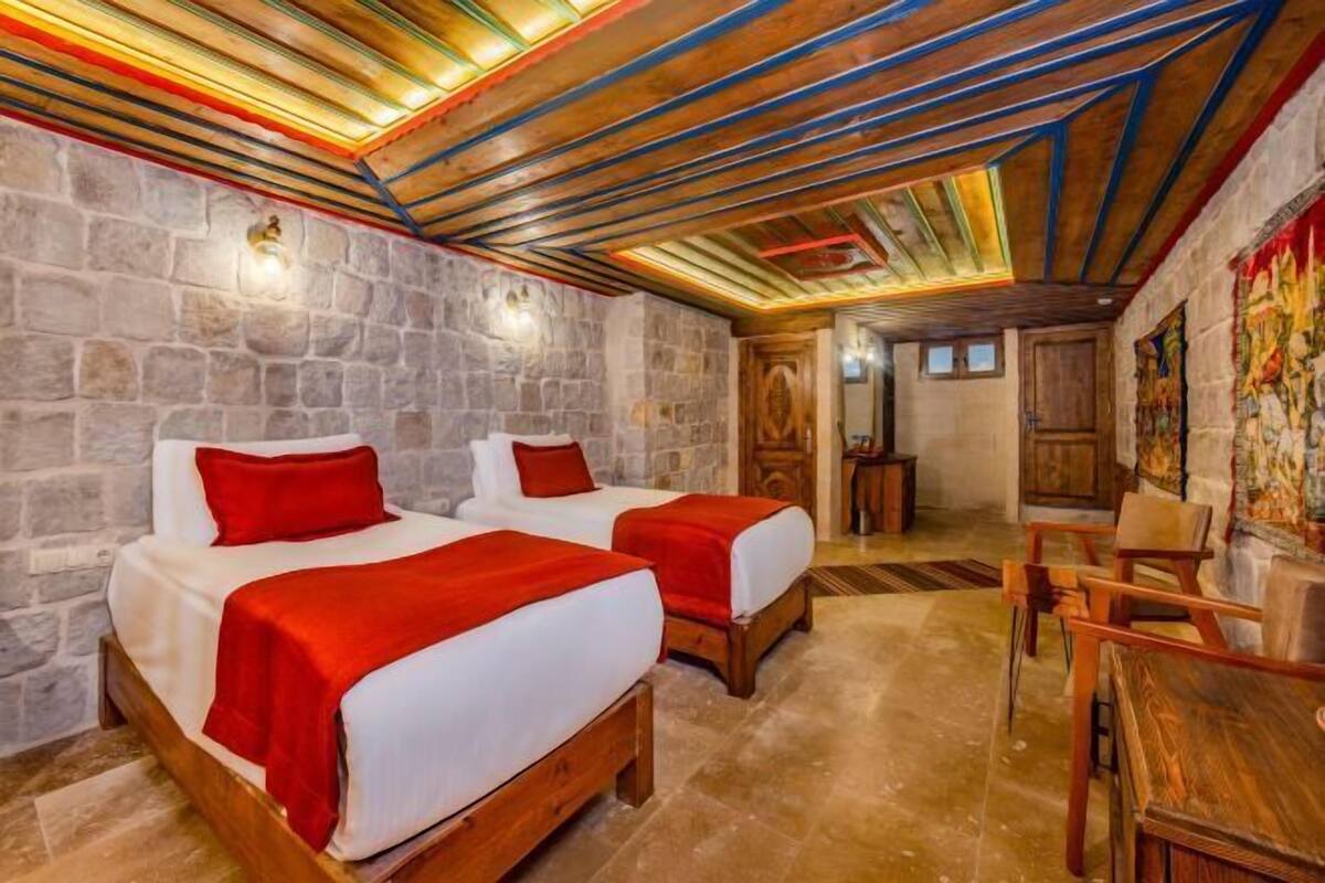 A room with two beds, stone walls, wooden beams, and a wooden table.