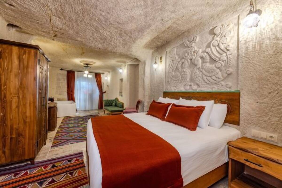 A bedroom with a large bed, a wooden wardrobe, a patterned rug, and a wall with carved artwork.