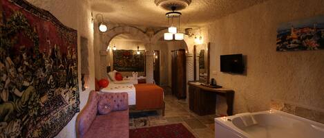 A room with a large bed, a sitting area with a sofa, a bathtub, and a wall-mounted TV.