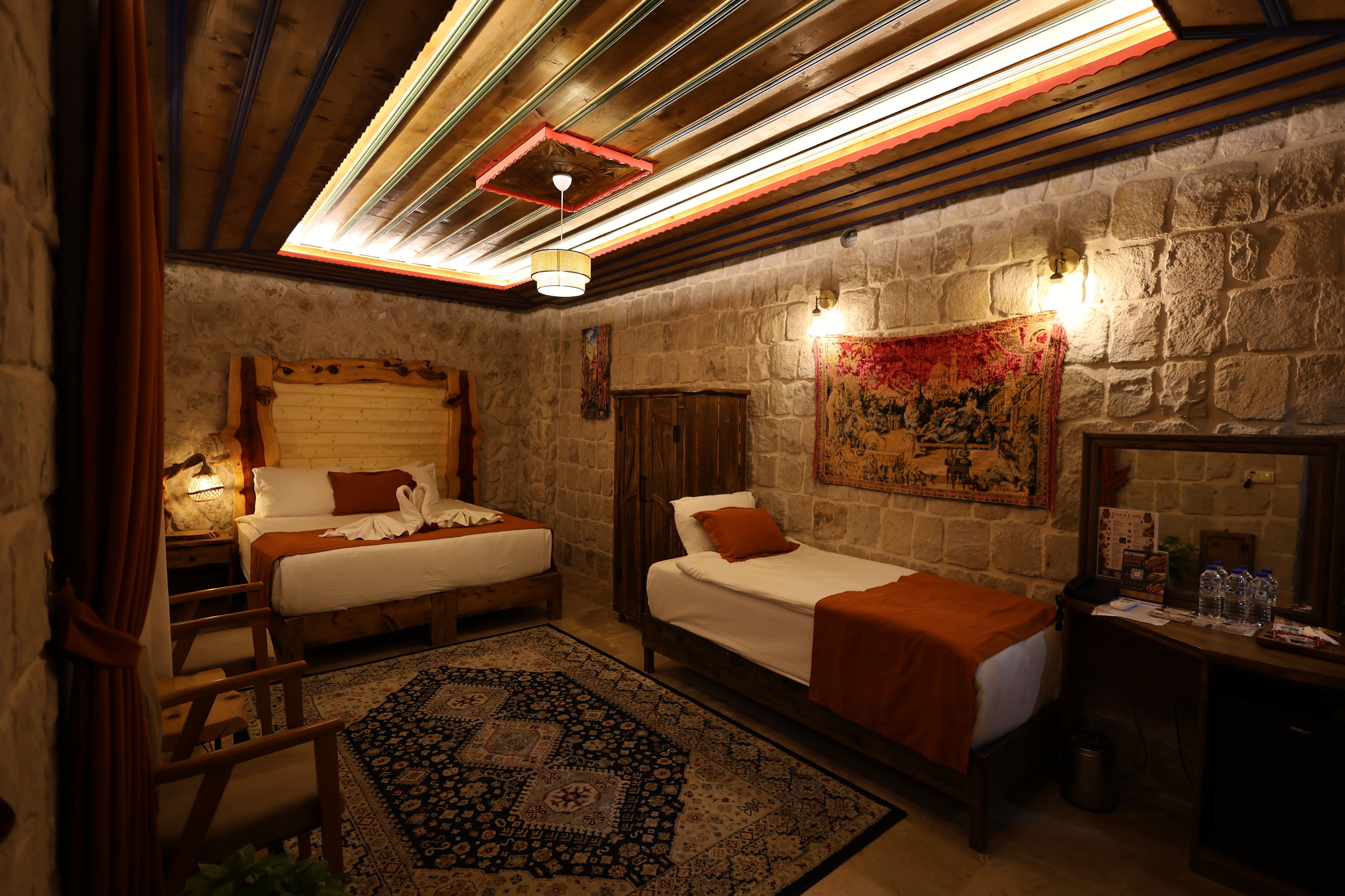 A room with two beds, a stone wall, a wooden ceiling, and a large tapestry.