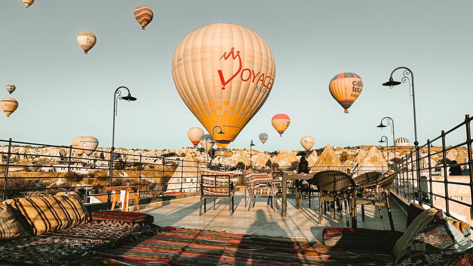 A rooftop terrace with hot air balloons, outdoor seating, and a view of a mountainous landscape.