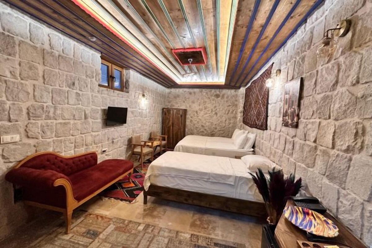 A stone-walled room with two beds, a red sofa, a wooden table, and a television.