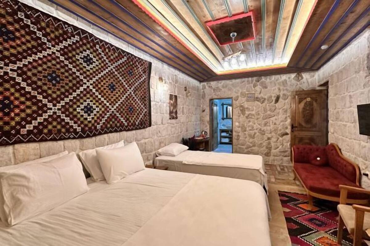 A room with a stone wall, a patterned tapestry, a bed, a red sofa, and a wooden door.
