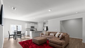 A modern living room with a sectional sofa, a red rug, and a dining area with a table and chairs.