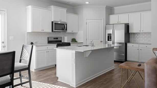 A modern kitchen with white cabinetry, a central island, stainless steel appliances, and a wooden dining table.