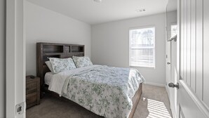 A bedroom with a wooden headboard, a bed with floral bedding, a nightstand, and a window with blinds.