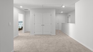 A hallway with a carpeted floor, white walls, and a double door at the end.