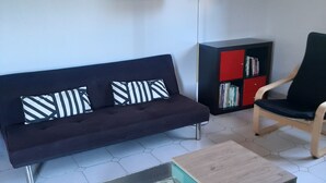 A modern living room with a dark sofa, a glass coffee table, a red bookshelf, and a black armchair.