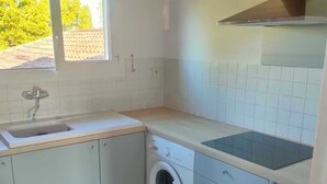 A compact kitchen with a washing machine, a sink, and a window with a view of trees.