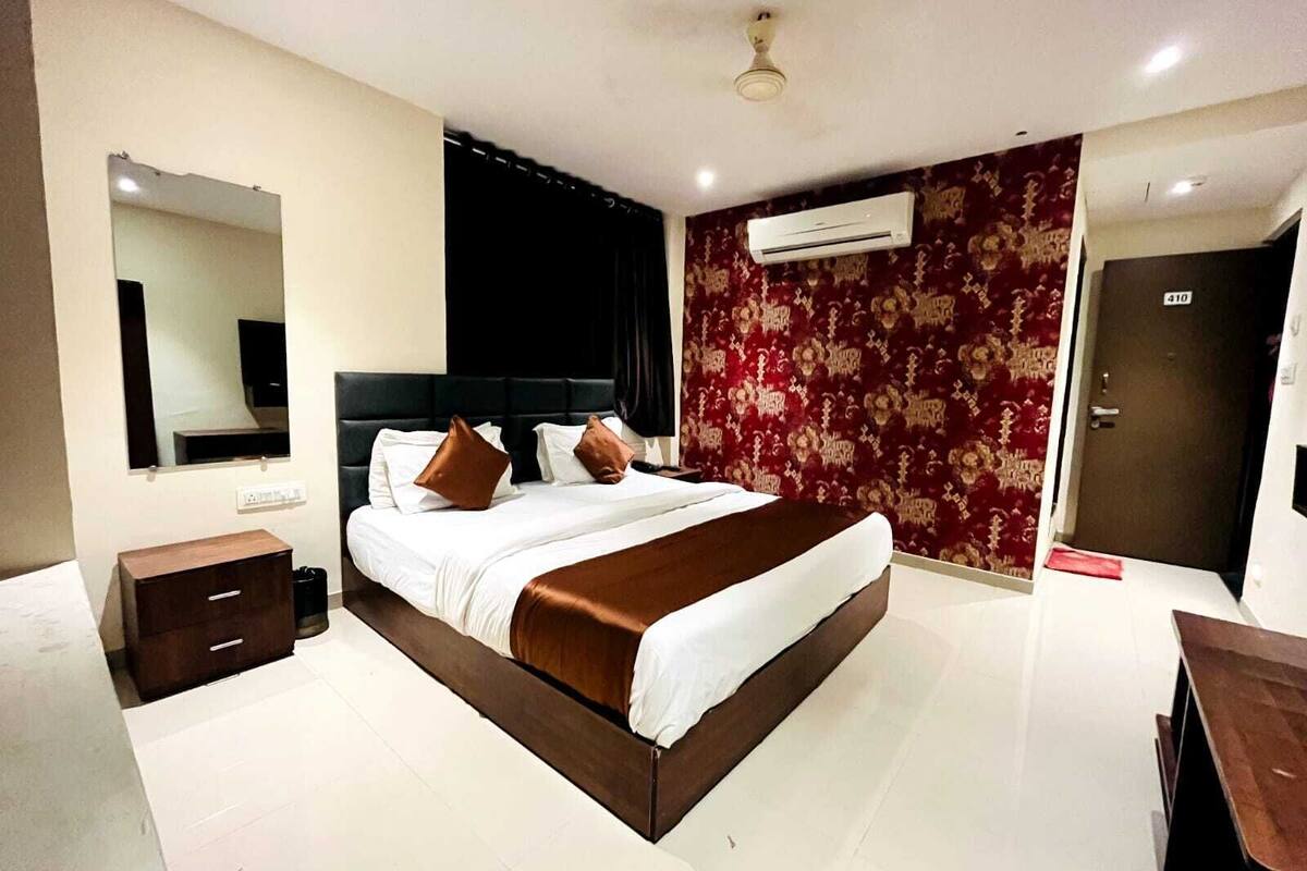 A modern hotel room with a large bed, a bedside table, a wardrobe, an air conditioning unit, and a door with a number.