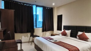 Habitación de hotel con una cama grande, escritorio, silla, televisión y ventana con cortinas.