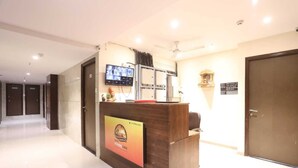 Een hotel receptie met een houten receptiebalie, een flatscreen televisie en een beveiligingscamera aan de muur.