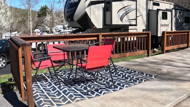 Un veicolo ricreativo (camper) con il logo 'Sandpiper', parcheggiato in un campeggio con un tavolo da picnic e sedie rosse.