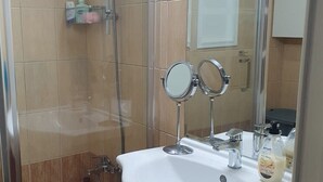 Un baño con ducha, lavabo con espejo e inodoro.