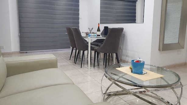 Una sala de estar moderna con una mesa de centro de vidrio, un sofá y un comedor con sillas y una mesa.
