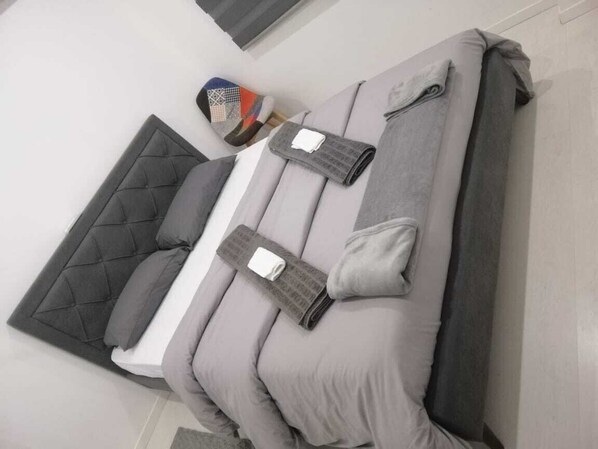 Un lit bien fait, avec une literie grise et une tête de lit matelassée.