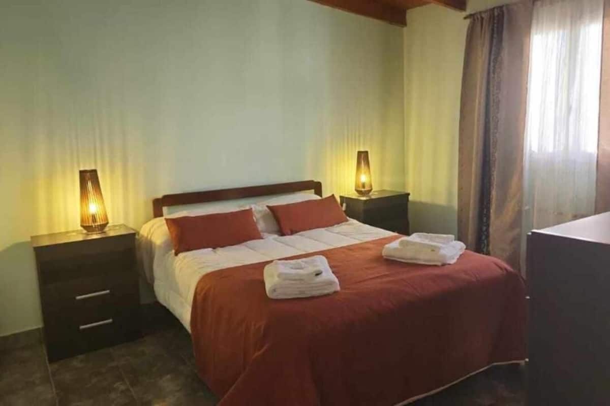 Habitación de hotel con cama, dos mesitas de noche, escritorio y ventana con cortinas.