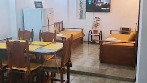 Ένα σαλόνι με τηλεόραση, έναν καναπέ, ένα τραπέζι φαγητού με καρέκλες και ένα κρεβάτι.