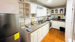 Una cocina con armarios blancos, un refrigerador de acero inoxidable, un fregadero, una estufa y un microondas.
