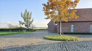 Un bâtiment en briques surmonté d’un toit en tuiles, entouré d’une allée pavée et d’un petit espace paysager agrémenté d’un arbre.