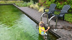 Un enfant dans une piscine, avec un plongeoir et des chaises à proximité.