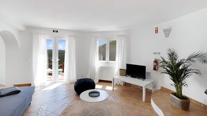 A modern living room with a sofa, a television, a potted plant, and a view of the outdoors.