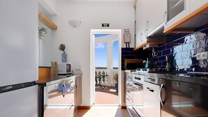 A narrow kitchen with white cabinets, a stainless steel stove, and a view through an open door to an outdoor patio.