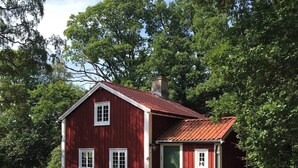 A red wooden cabin with a green door, surrounded by trees. - Cottage for Rent in Urshult (Urshult)