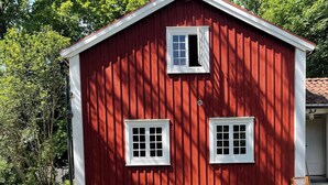 A red barn with two windows and a table with six chairs in front. - Cottage for Rent in Urshult (Urshult)