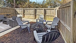 Eine Außenpatio mit Adirondack-Stühlen, einer Feuerstelle und einem kleinen Tisch.