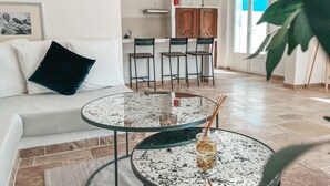 A modern living room with a white sofa, a round glass coffee table, and a dining area with wooden cabinets and chairs.