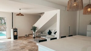 A modern interior with a large kitchen island, a dining area with a round table, and a staircase leading to a lofted seating area.